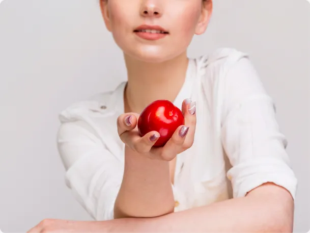 A woman in a white shirt holding a fresh red apple